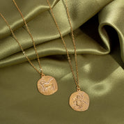 Two gold necklaces with circular pendants on a green satin surface