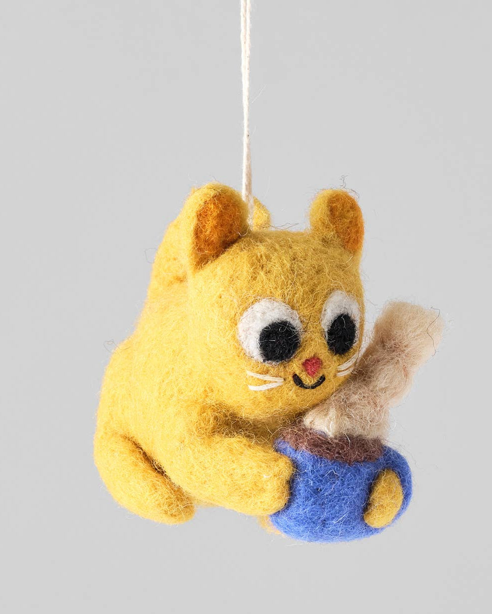 Yellow cat-shaped plush toy holding a blue ball, hanging against a gray background.